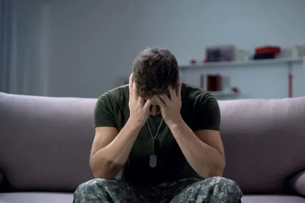 5 Causes of Post-Traumatic Stress Disorder a man slumped over on his couch with his face in his hands suffering from post traumatic stress disorder