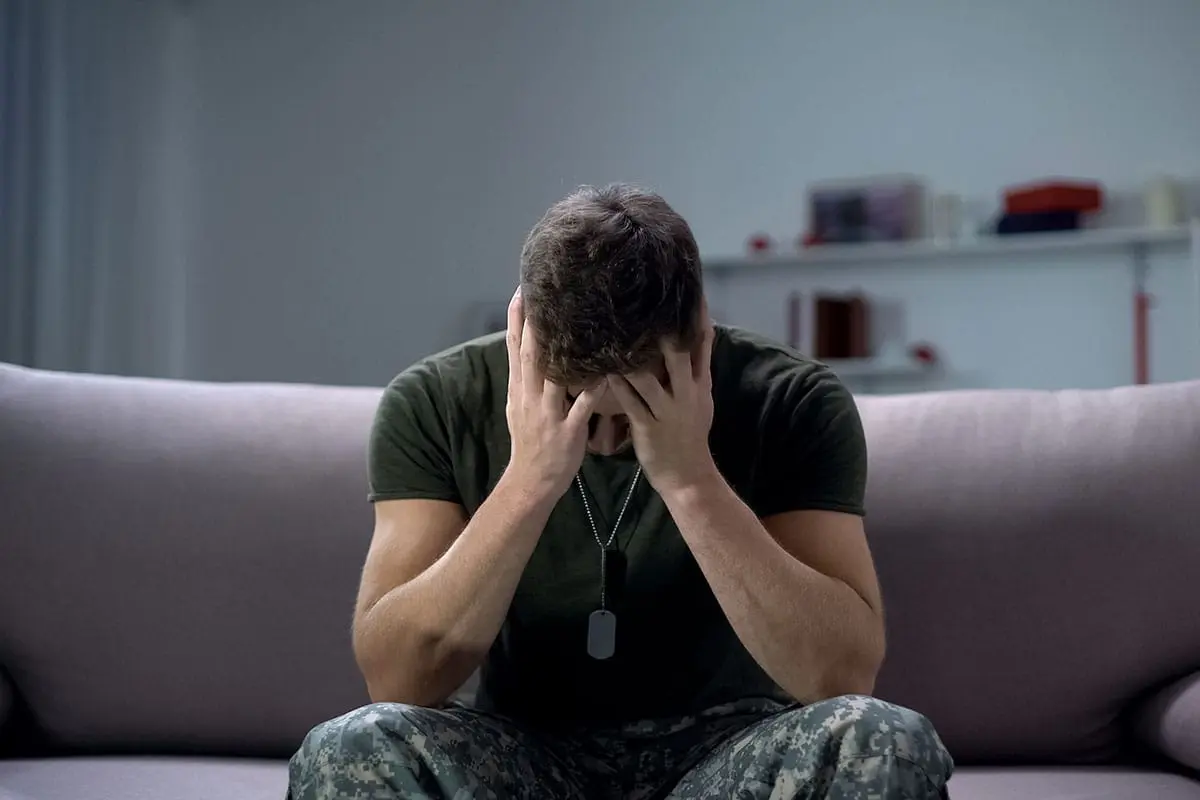 5 Causes of Post-Traumatic Stress Disorder a man slumped over on his couch with his face in his hands suffering from post traumatic stress disorder