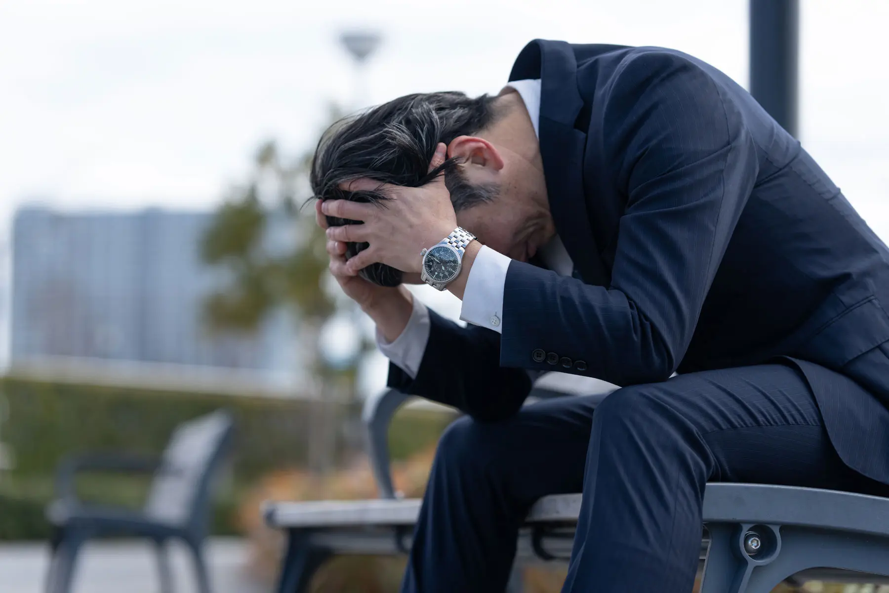 Long-Term Effects of Anxiety a person in a suit sits on an outdoor bench with their head in their hands while dealing with the long term effects of anxiety
