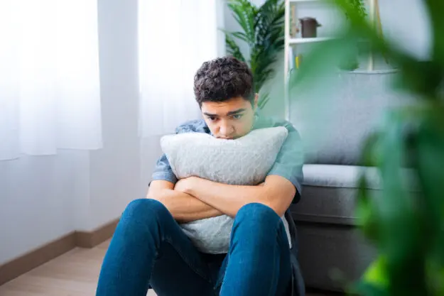 What Happens if Bipolar Disorder Goes Untreated a person sits on the floor and hugs a pillow while dealing with untreated bipolar disorder