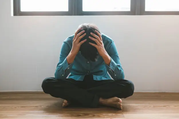 What Should I Do After Self-Harm Relapse a person sits on the floor and puts their hands on their head after a self harm relapse