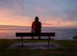 a man feels lonely to the point of it affecting his mental health as he sits alone on a bench at dusk