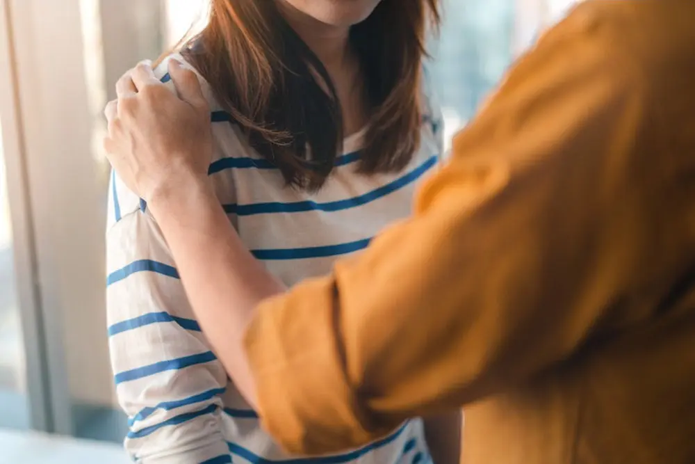 a woman touching her adult daughter's shoulder while encouraging her to seek mental health treatment