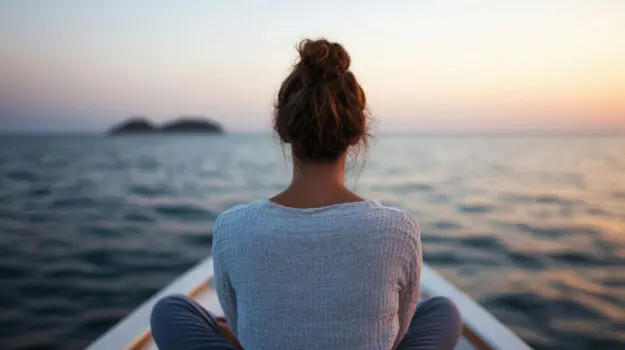 A woman is watching the sunrise on the water in a peaceful outdoor setting.
