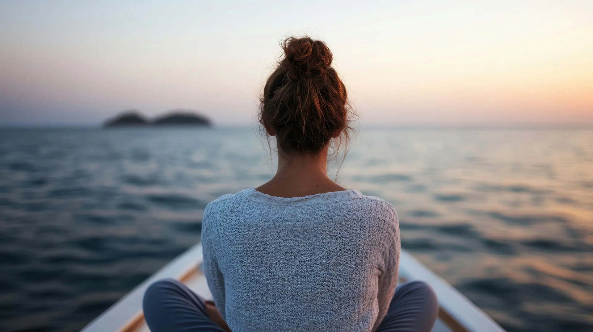 A woman is watching the sunrise on the water in a peaceful outdoor setting.