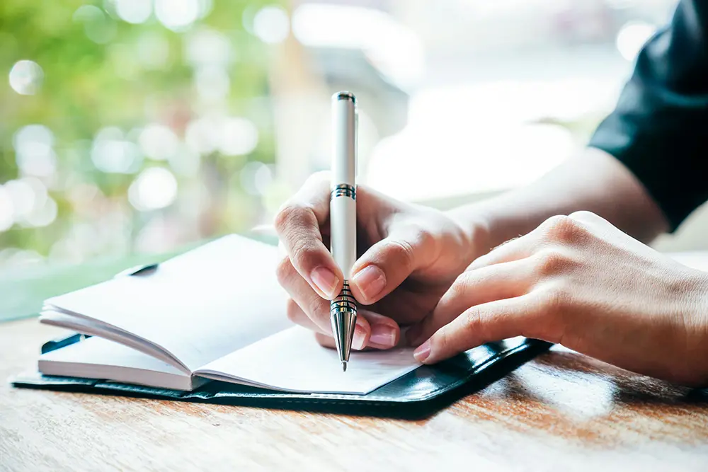 Person writing in a journal at a small table, reflecting on thoughts and feelings.