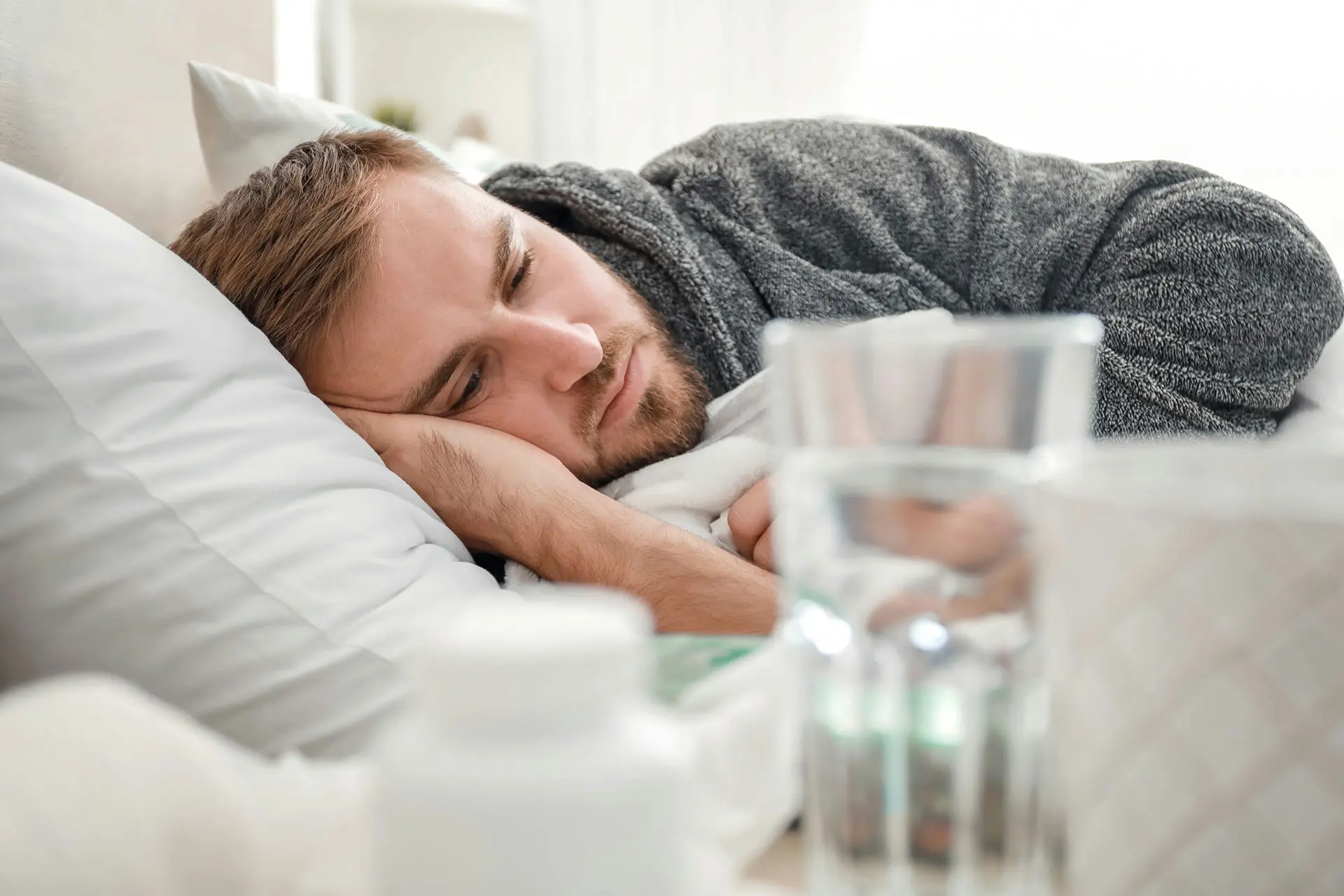 Man having mental breakdown laying in bed next to water and medication on a bedside table.