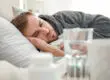 man having mental breakdown laying in bed next to water and medication on a bedside table