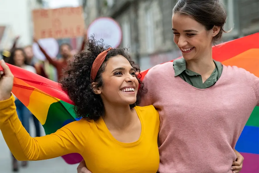 Two woman giving side hugs during LGBT pride parade.