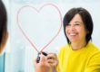 a woman draws a lipstick heart around her reflection in the mirror