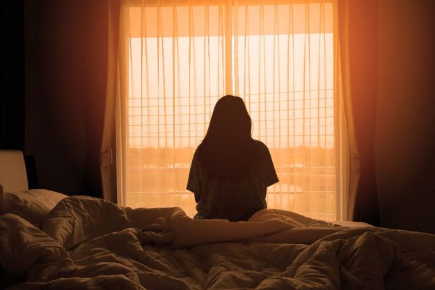 a woman sitting on her bed looking out her window thinking about insurance for mental health