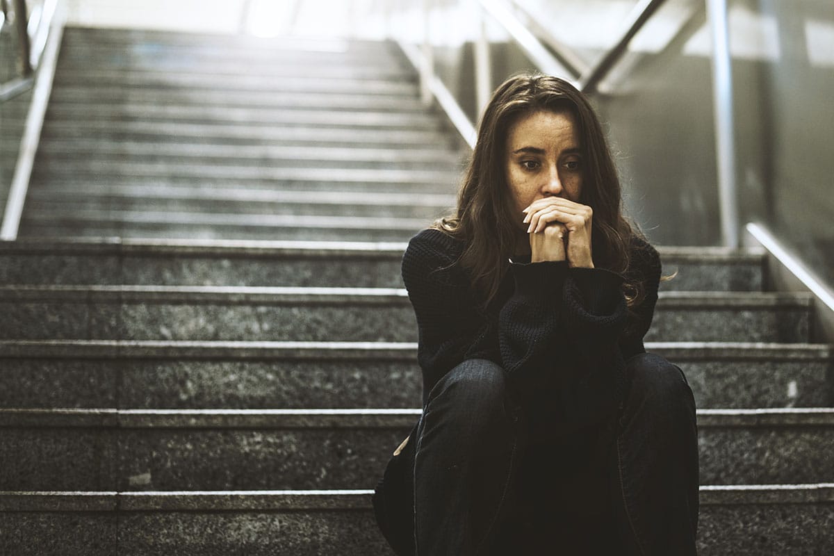 a woman sitting on a staircase thinking about self harm awareness
