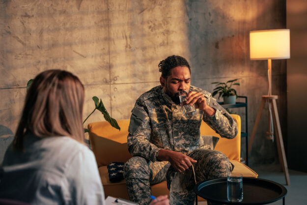 a veteran in fatigues drinks a glass of water in therapy to show anxiety in veterans