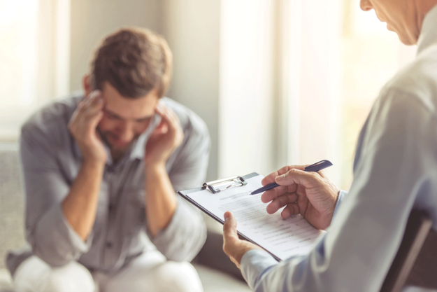 a person puts their fingers on their temples as they talk to a therapist about the signs of a narcissist