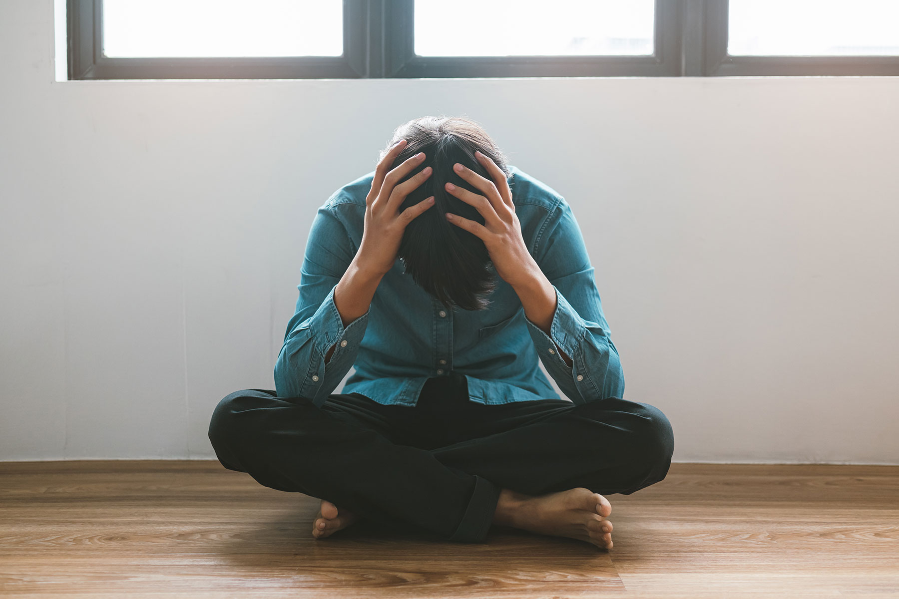 a person sits on the floor and puts their hands on their head after a self harm relapse