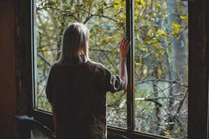 a woman struggling with mental health relapse stares out of a window 