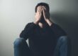 a man hides his face in his hands as he struggles with self harm behaviors