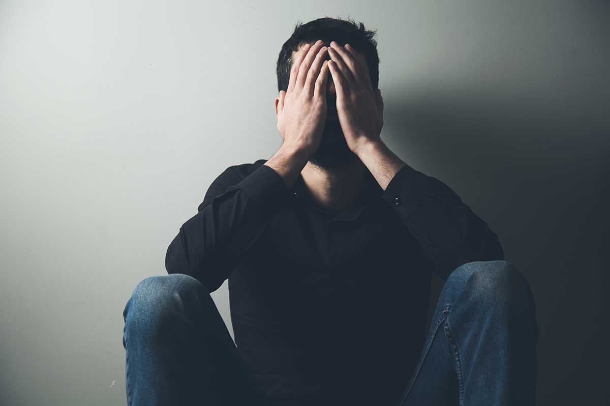 a man hides his face in his hands as he struggles with self harm behaviors