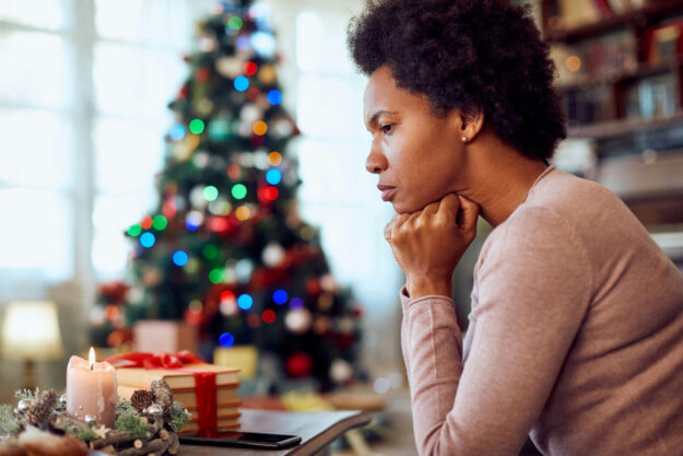 A person sitting quietly beside soft holiday lights, reflecting on feelings of holiday loneliness.