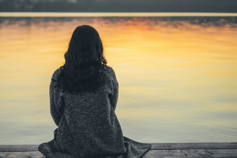 Person sitting quietly outdoors reflecting while coping with grief and loss after a life change.